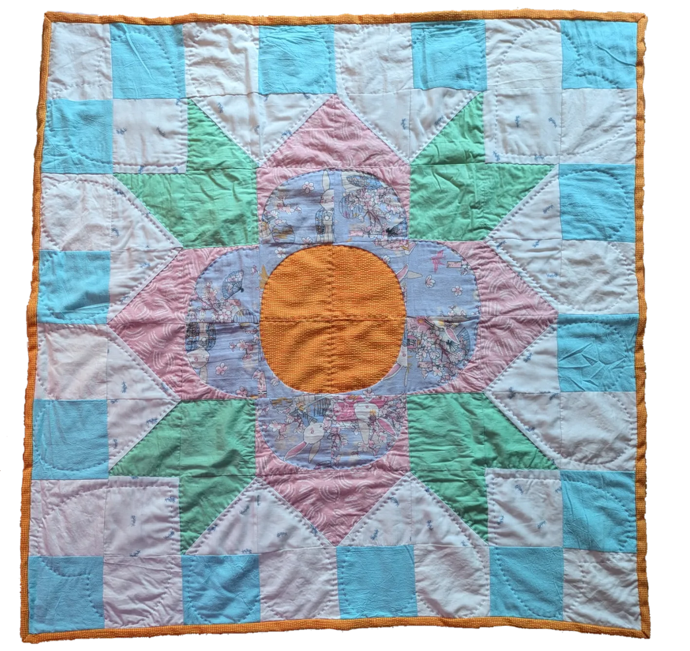 Small square quilt photographed against a black background, featuring a starburst star block pattern in pastel cotton fabrics — light blue, mint green, pink, and orange patches with visible hand quilting stitches and an orange border
