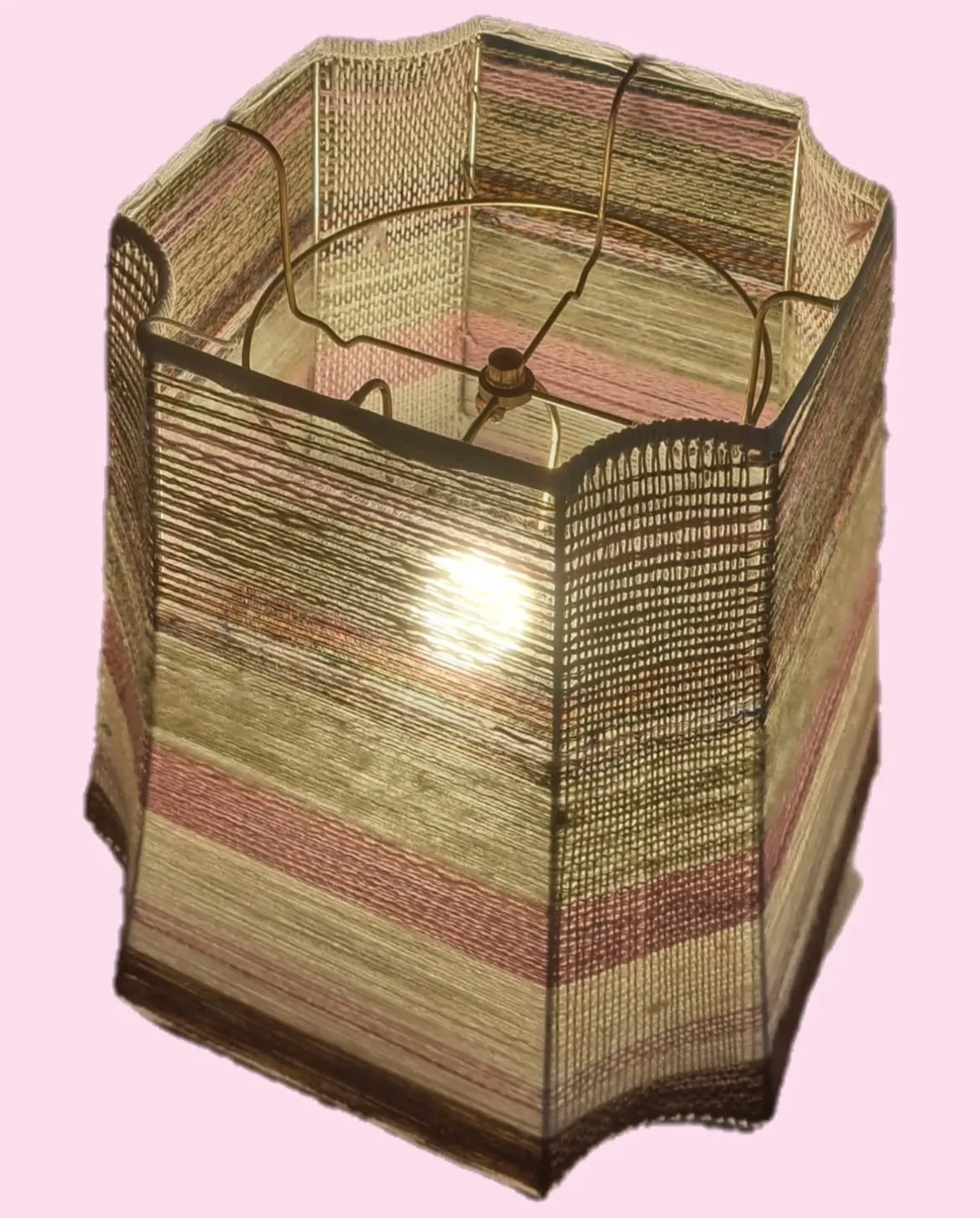 Hexagonal lamp shade sculpture made from a wire frame wrapped with horizontal stripes of natural, cream, and dusty rose hand-spun yarn, illuminated from inside against a pink background